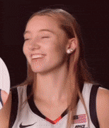 a woman in a basketball uniform is smiling with her eyes closed while holding a sign .