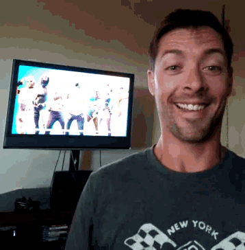 a man wearing a new york t-shirt smiles in front of a television