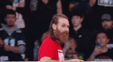 a man with a beard wearing a red shirt is standing in front of a crowd .