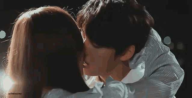 a man and a woman are kissing in front of a dark background .