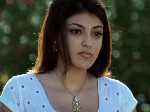 a woman wearing a white top and a necklace looks at the camera