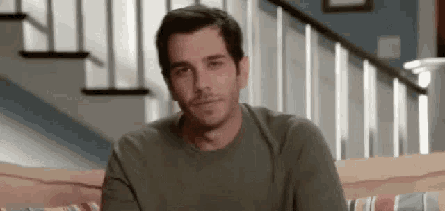 a man in a green shirt is sitting on a couch in front of a staircase .