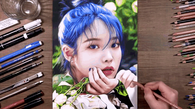 a person is drawing a picture of a woman with blue hair surrounded by colored pencils .
