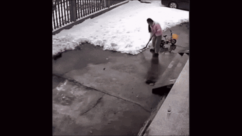 a man is shoveling snow in a driveway with a bicycle in the background