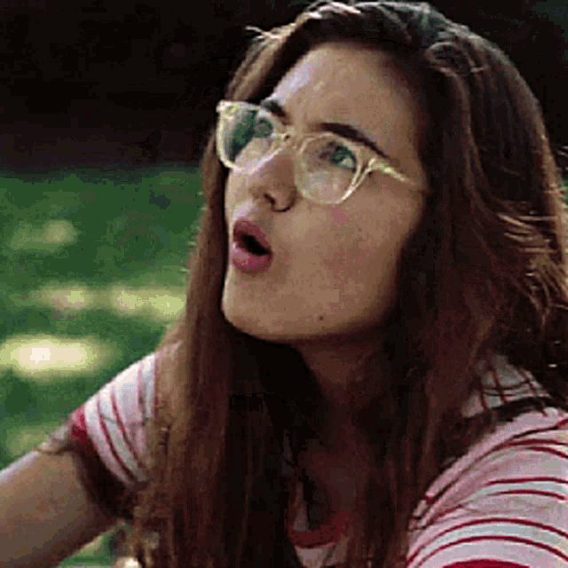 a woman wearing glasses and a striped shirt is making a face