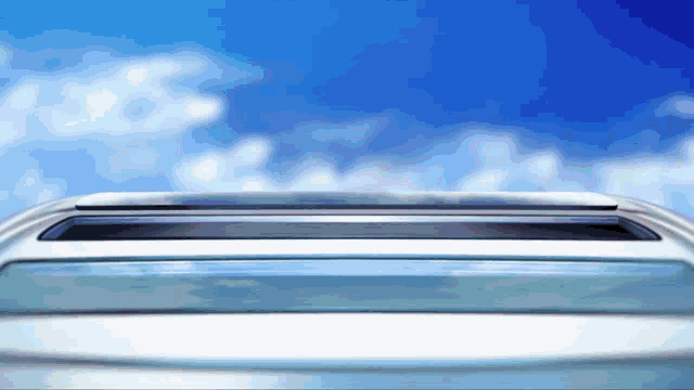 a car with a sunroof open against a blue sky with clouds