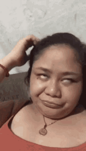 a woman wearing a red tank top and a necklace is making a funny face while scratching her head .