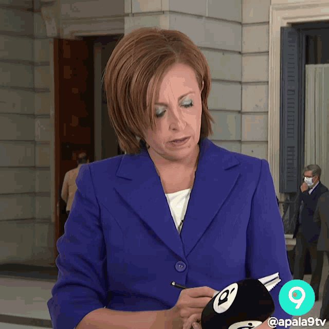 a woman in a blue suit is writing on a microphone with the number 9 on it