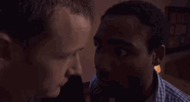 two men are looking at each other in a dark room and one of them is drinking from a glass .