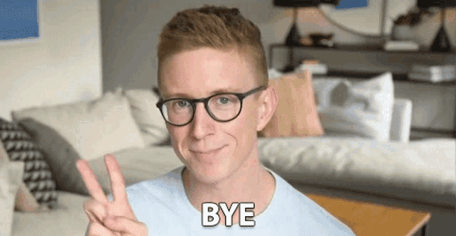 a man wearing glasses is giving a peace sign and the word bye is behind him .