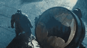 a man in a superhero costume is standing next to a large barrel .