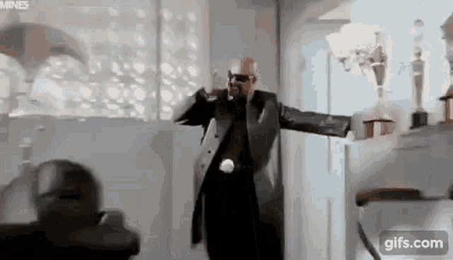 a man in a suit and sunglasses is dancing in a living room .