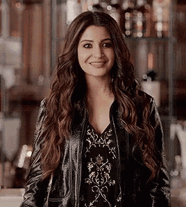 a woman with long wavy hair is wearing a black leather jacket and a black dress .
