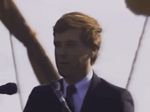 a man wearing a suit and tie is speaking into a microphone