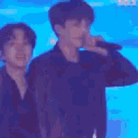 a man is singing into a microphone while standing next to another man on a stage .