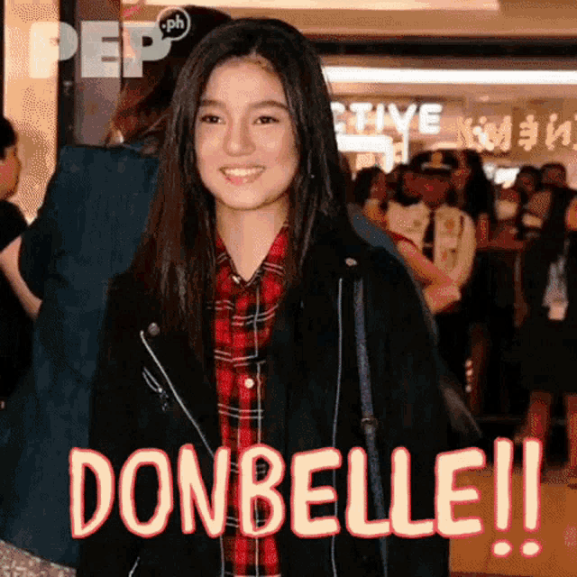 a woman in a plaid shirt and a black jacket is standing in front of a crowd and says donbelle !