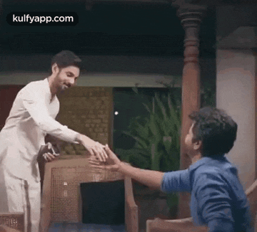 a man is giving a gift to another man while sitting in a chair .