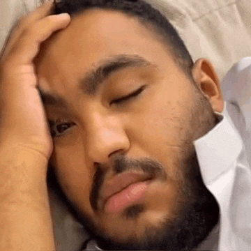 a man with a beard is laying on a bed with his hand on his head .