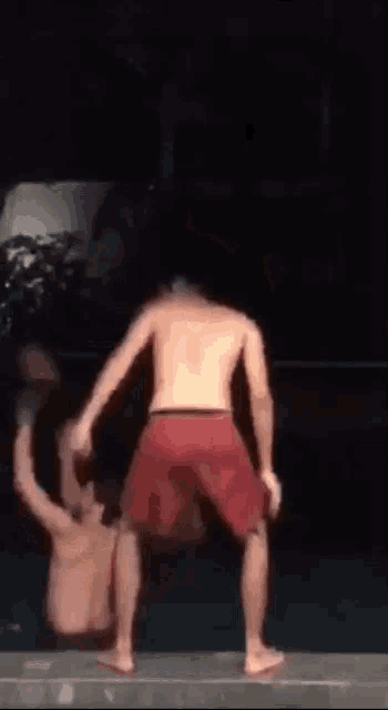a man in red shorts is giving a thumbs up while another man is falling into a pool .