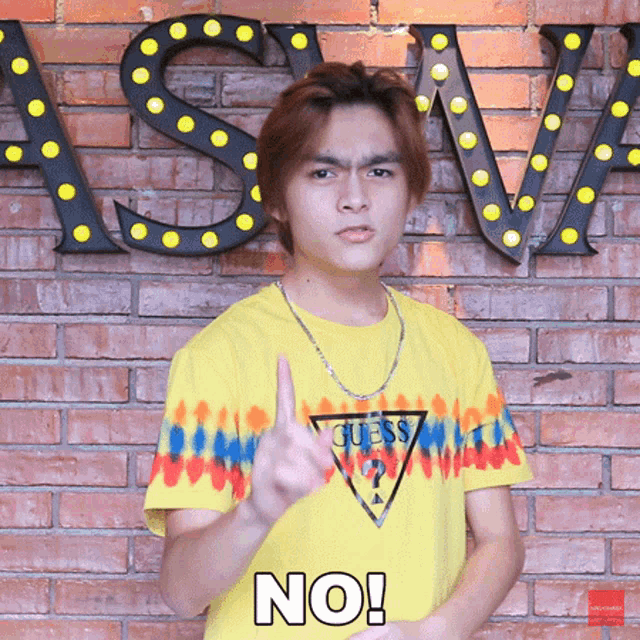a young man wearing a yellow guess shirt is making a no sign