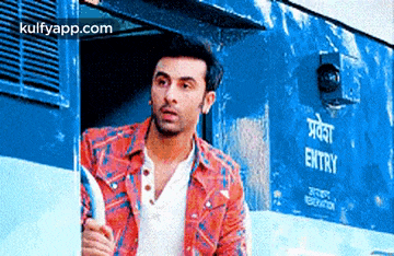 a man in a red and blue shirt is standing in front of a blue train .