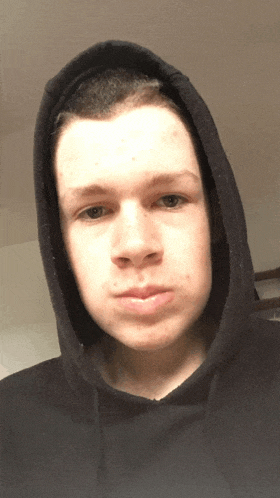 a young man wearing a black hooded sweatshirt looks at the camera