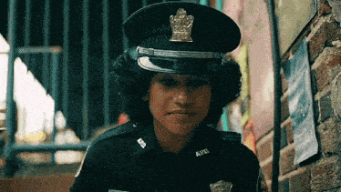 a young woman in a police uniform is standing next to a brick wall and looking at the camera .