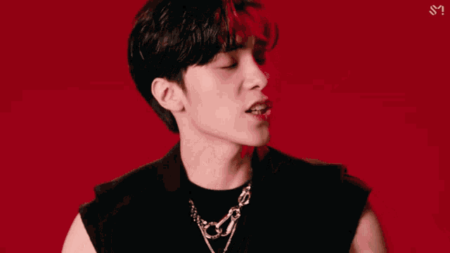 a man in a black vest and necklace is making a face