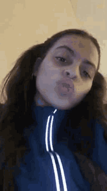 a young woman is blowing a kiss while wearing a blue jacket .