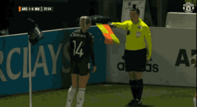 a female referee stands next to a man in a yellow shirt during a game