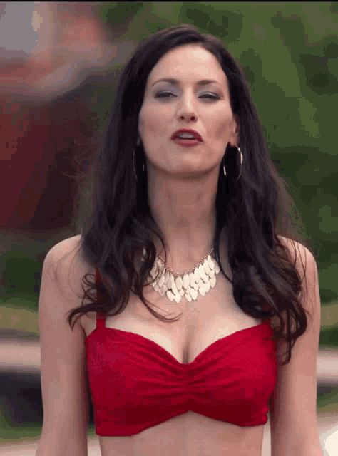 a woman wearing a red top and a gold necklace looks at the camera