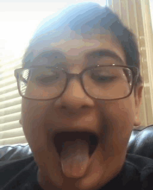 a boy wearing glasses is sticking out his tongue