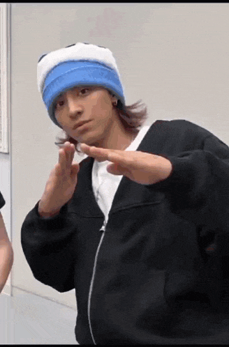 a man wearing a blue and white hat and a black jacket is making a peace sign with his hands .