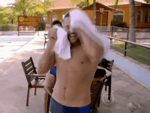 a shirtless man holds a towel over his head