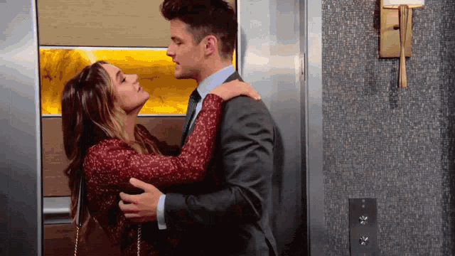 a man in a suit and a woman in a red dress kiss in an elevator