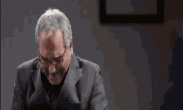 a man in a suit and glasses is holding a piece of paper in front of his face .