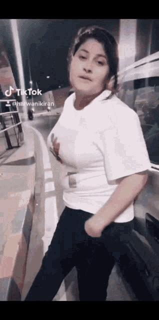 a woman wearing a white t-shirt and black pants is standing in front of a car and a sign that says tik tok