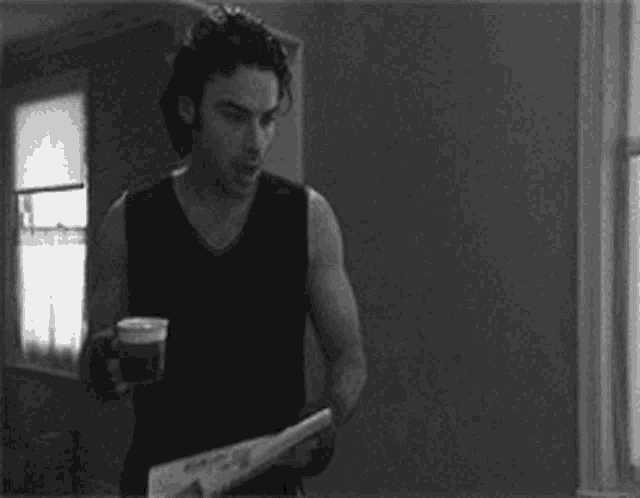 a man is drinking a cup of coffee and reading a newspaper .