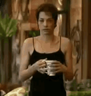 the woman is wearing a black tank top and holding a cup of coffee .