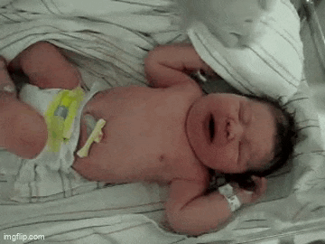 a newborn baby is crying while laying on a bed .