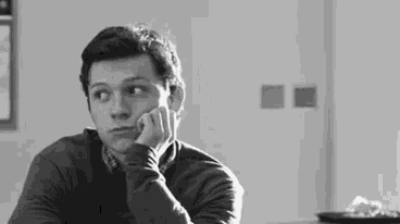 a black and white photo of a man sitting at a table with his head resting on his hand .