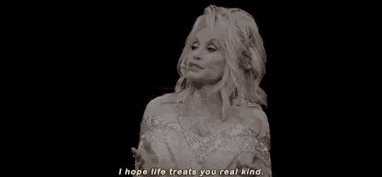 dolly parton is wearing a white dress and talking into a microphone while standing on a stage .