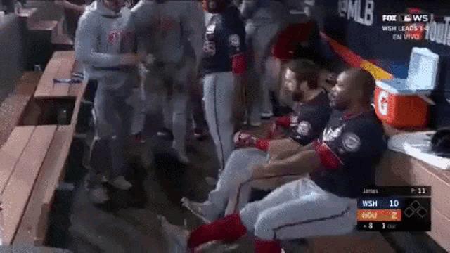 a group of baseball players are sitting on a bench in a dugout during a game .