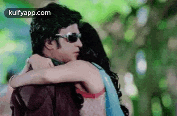 a man and a woman are hugging each other . the man is wearing sunglasses and the woman is wearing a bra .