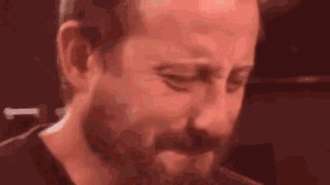 a close up of a man with a beard crying in a crowd .