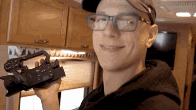 a man wearing glasses and a hat holds a camera