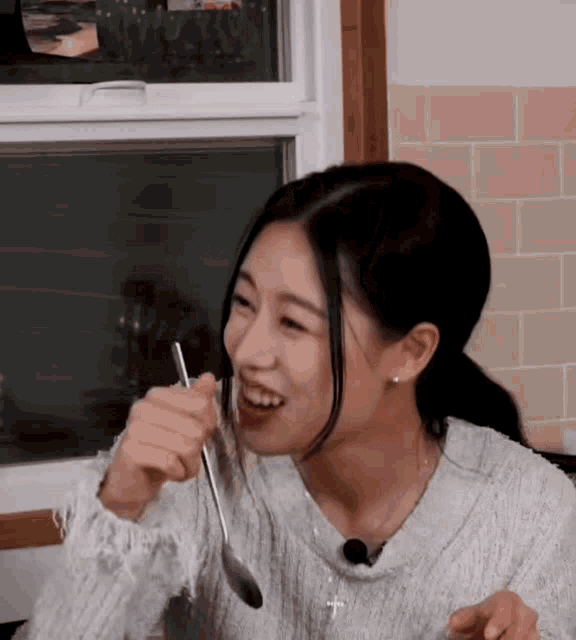 a woman in a white sweater is holding a spoon in her hand and smiling .