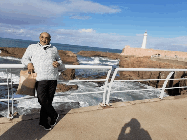 a man in a grey sweater is standing on a ledge overlooking the ocean