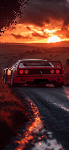 a red ferrari sports car is driving down a road at sunset
