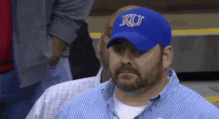 a man wearing a blue ku hat looks to his left